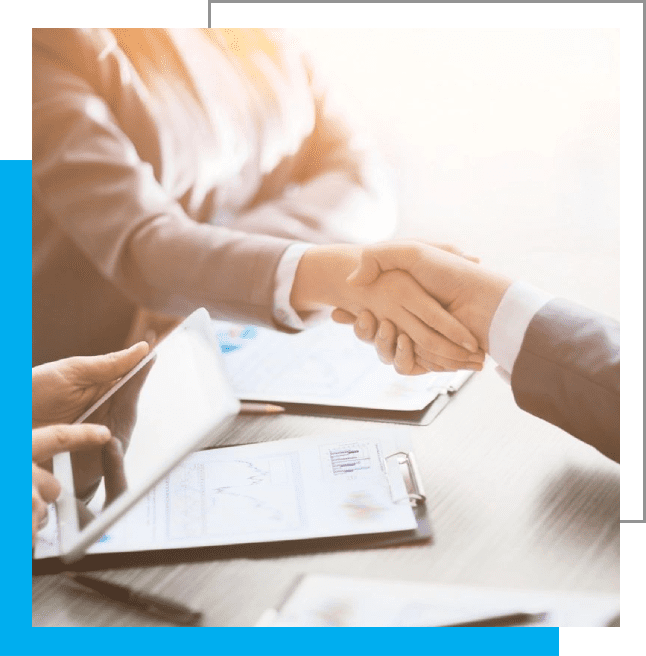 Two people shaking hands over a table with papers.