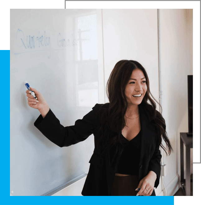 A woman in black jacket writing on white board.